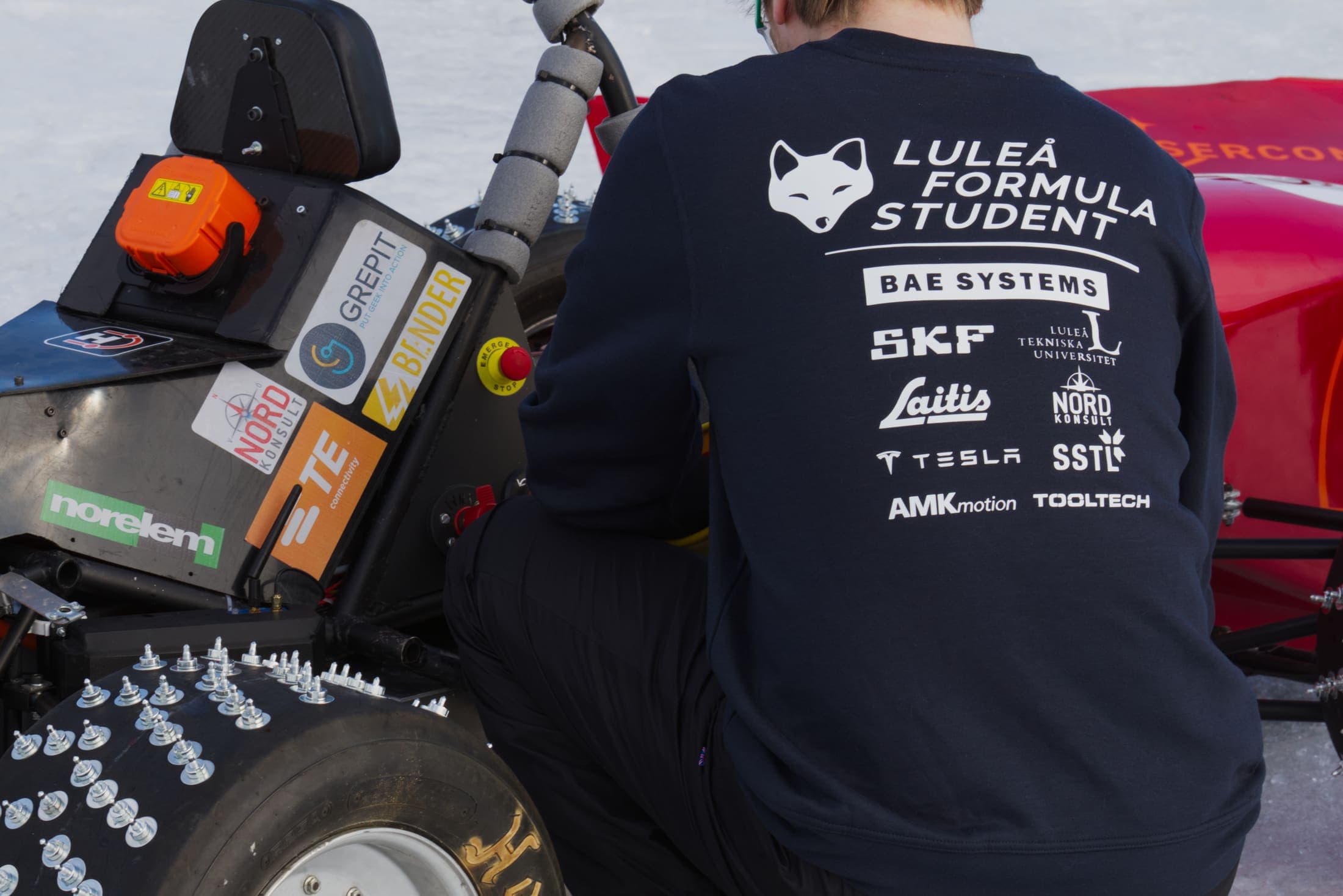 LFS-medlem i teamtröja med sponsorlogotyper, framför bilen